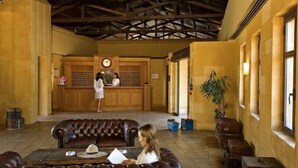 A lobby with a leather sofa, wooden reception desk, and a large plant. - Miramare Park (Rhodes)