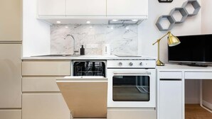 A modern kitchen with white cabinetry, a built-in oven, and a microwave. There is a hexagonal wall decoration and a gold lamp on the countertop. - Modern Studio | Parking | Close to the Airport (Warszawa)