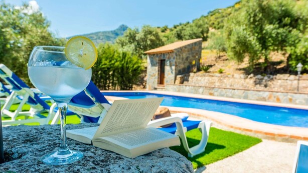 Un entorno junto a la piscina con vista despejada, sillas de descanso y un edificio de piedra al fondo.