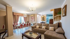 Ein geräumiges Wohnzimmer mit einer Couch, einem Esstisch mit Stühlen und einer Chandelüster.