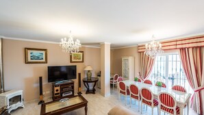 Ein Wohnzimmer mit Fernseher, Unterhaltungseinheit und Essbereich mit gestreiften Stühlen und einer Kandelaber.