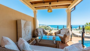 Ein Balkon mit Korbmöbeln, einem Glastisch und Buddha-Statuen.