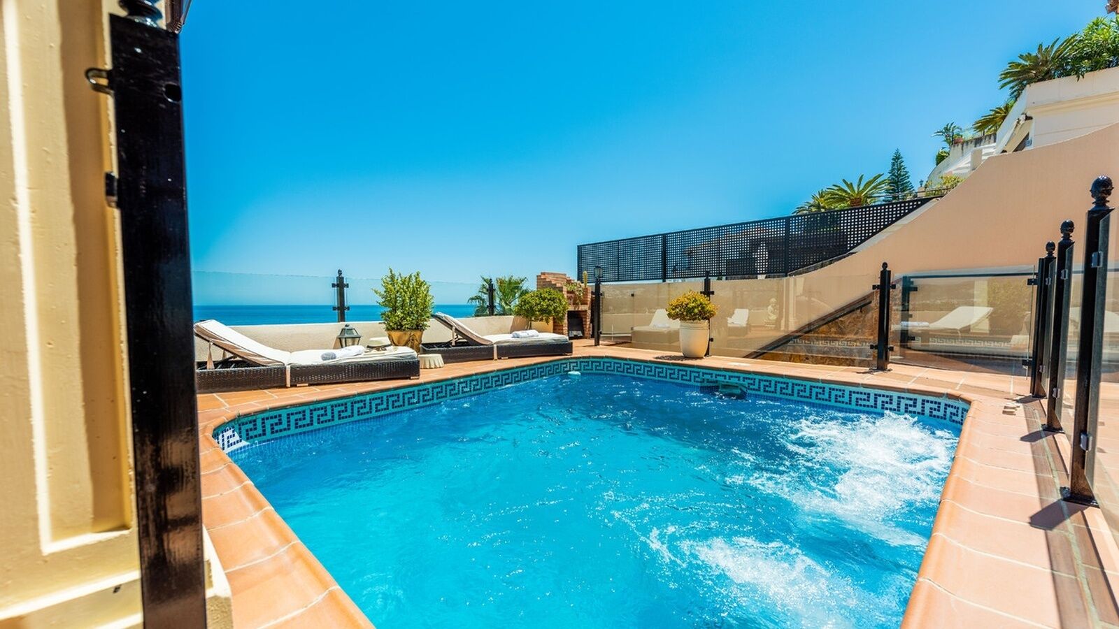 A swimming pool with a clear view of the ocean, surrounded by lounge chairs and potted plants.