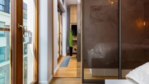 A modern hotel room with a large sliding glass door, a wooden floor, and a view of the cityscape. - Modern Studio in the Center | Balcony | Close to Attractions (Warszawa)