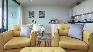 Una sala de estar moderna con dos sofás, una mesa de centro de vidrio y un comedor con una silla y mesa blancos.