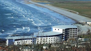 Un edificio frente al mar con techo curvo, junto a una playa con olas.