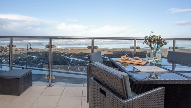 Un balcón con una mesa de vidrio, sillas de mimbre y vistas a la playa y al océano.