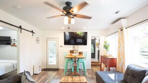 Una sala de estar moderna con un sofá, una mesa de centro, una mesa de comedor con sillas, un ventilador de techo y un televisor montado en la pared.