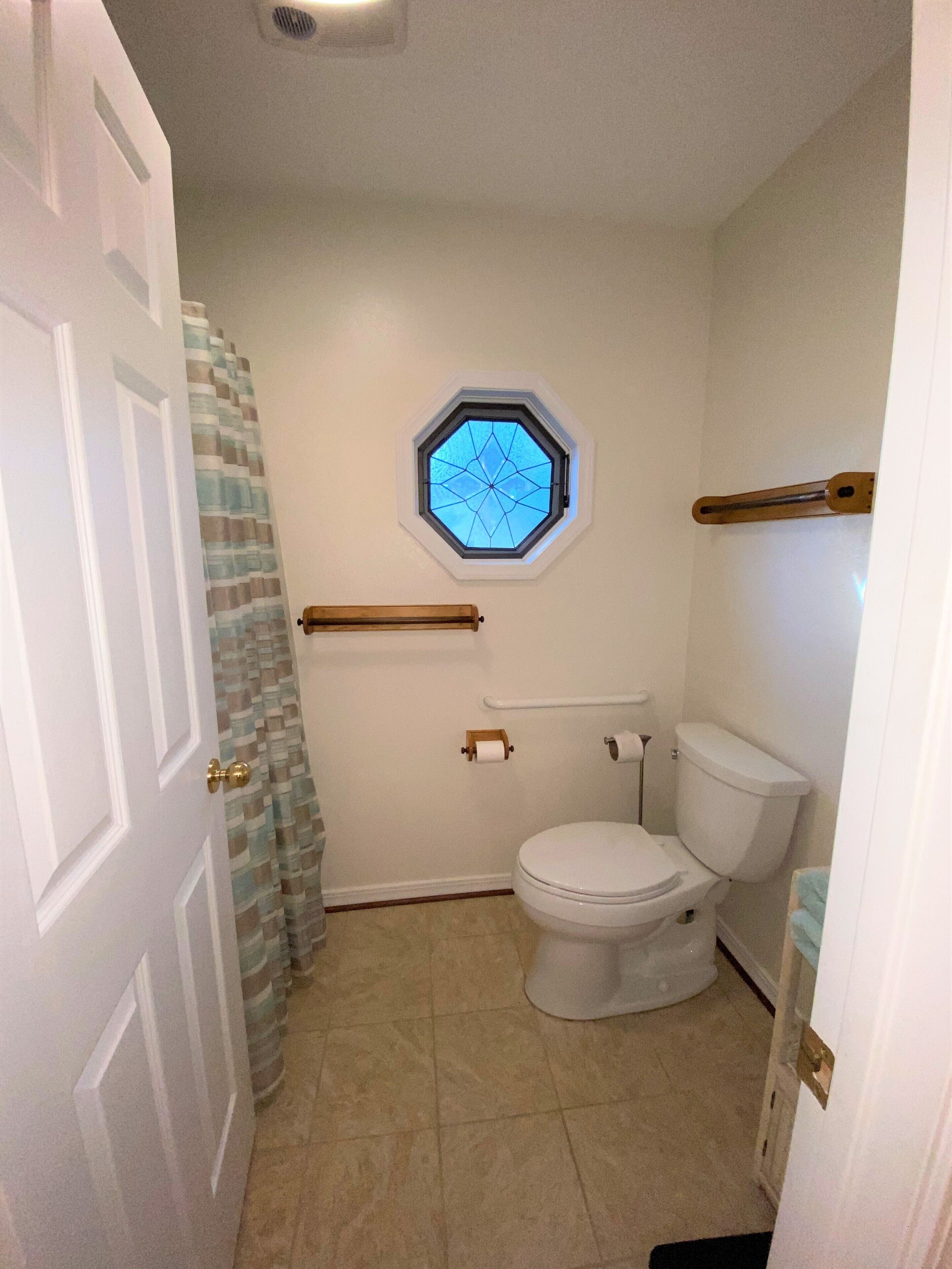 A bathroom with a white toilet, a window with a geometric pattern, a towel rack, and a shower curtain.