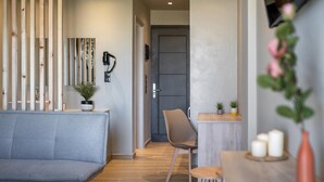 A modern room with a grey sofa, a wooden partition, a small table with candles, and a potted plant. - Nicolas Grand Suites (Kos)