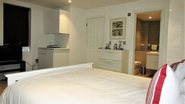 A bedroom with a large bed, a television, a desk, and a bathroom visible through an open door. - Stylish Private Double En-suite - 1 (London)
