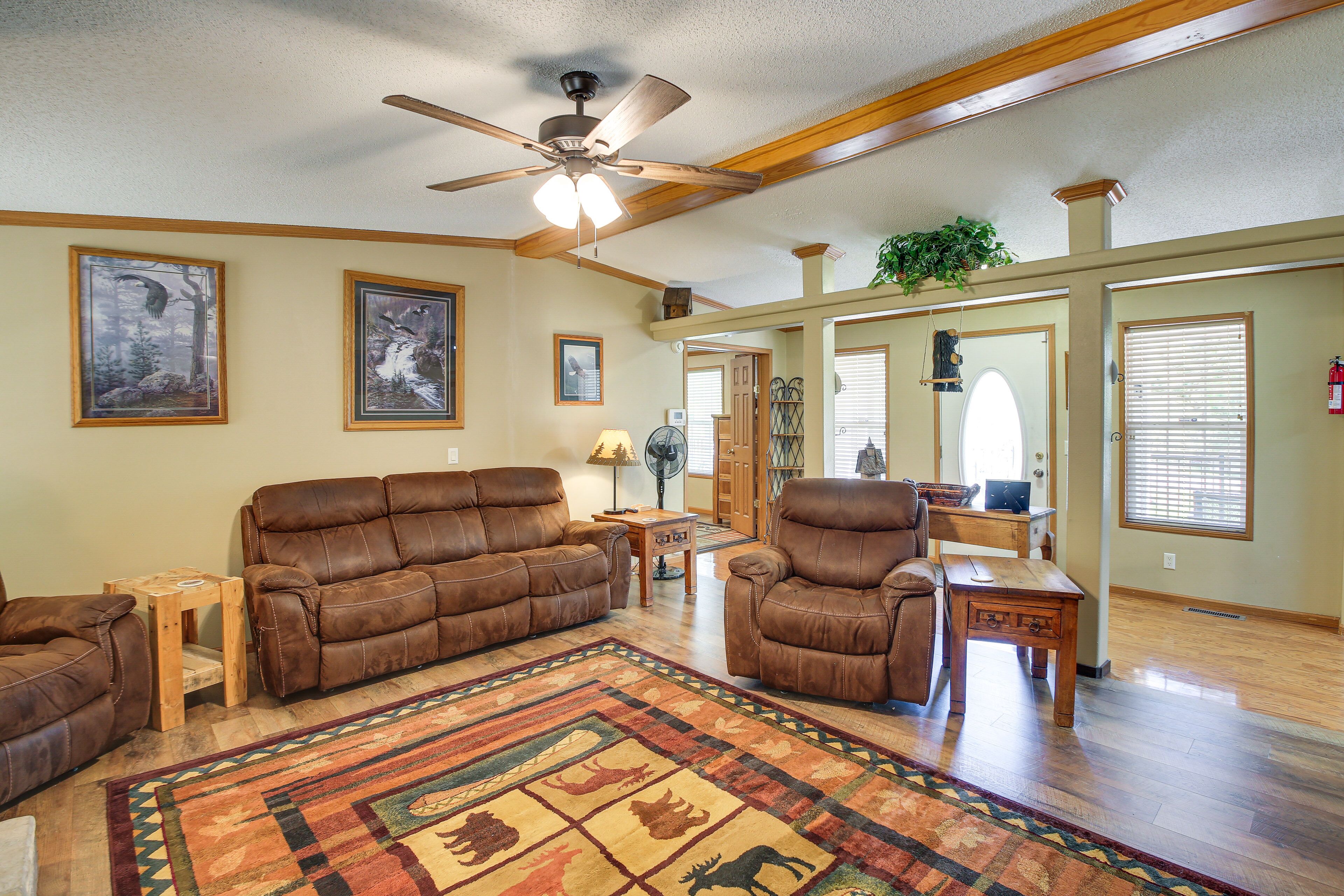 A spacious living room with a ceiling fan, two leather sofas, a wooden coffee table, and a patterned rug.