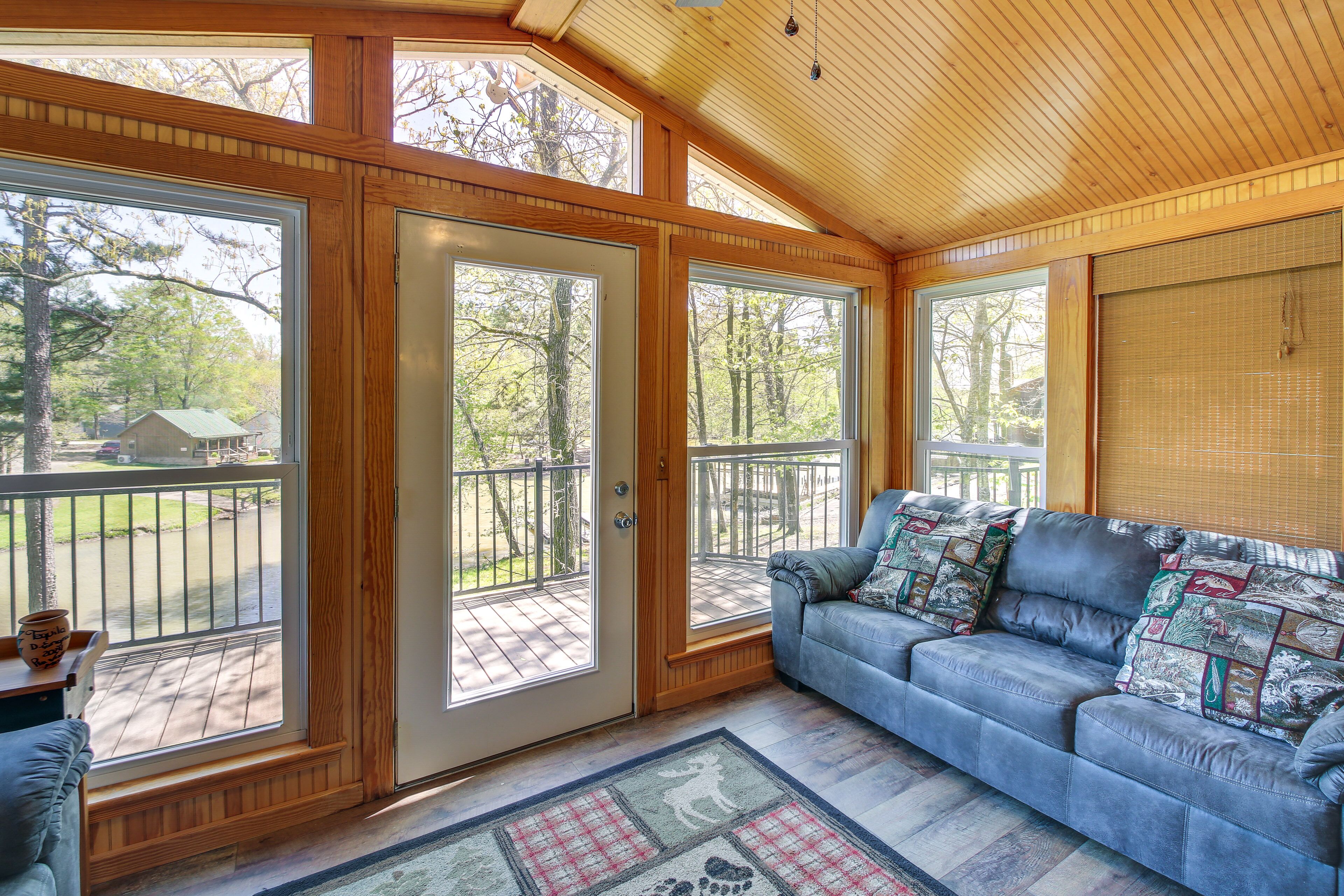 A cozy room with a large window, a sofa with patterned cushions, and a wooden ceiling.