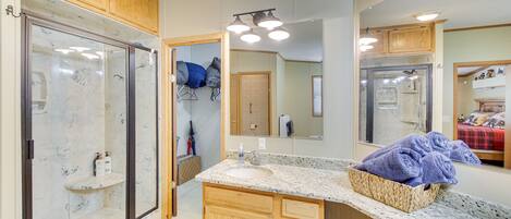 A bathroom with a glass shower enclosure, wooden cabinets, a granite countertop, and a large mirror.