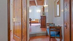 Uma porta de madeira dá acesso a uma sala de estar com um sofá, uma poltrona e um armário.
