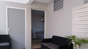 Quarto com sofá preto, uma mesinha, uma planta em vaso e porta que dá para outro cômodo.