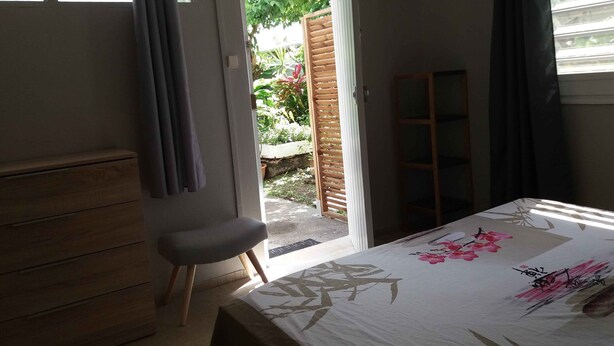 Quarto com cama, poltrona, cômoda de madeira e janela com cortinas.