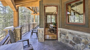 Una terraza de madera con paredes de piedra, un comedor con candelabro y vistas al bosque.
