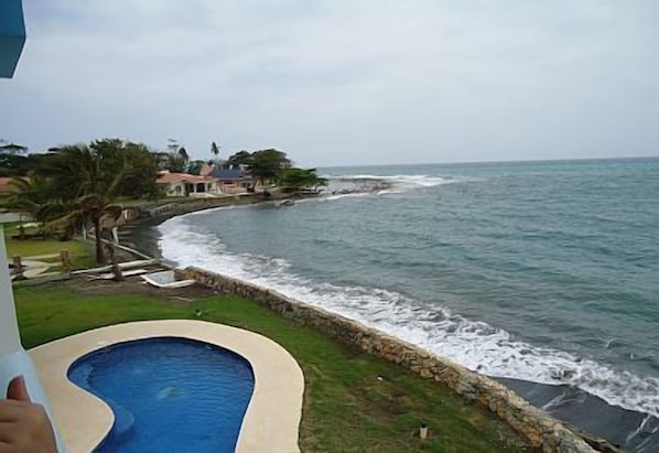 A coastal view with a swimming pool, a stone wall, and a beach.