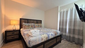A bedroom with a bed, a nightstand, a lamp, a window with curtains, and a chair. - Universal Studios, International Dr (Orlando)