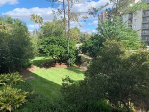 Un jardin luxuriant, avec une grande variété d’arbres et d’arbustes, un chemin bien tracé et un bâtiment visible au loin.