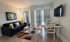 A living room with a sofa, coffee table, dining table, chairs, a TV, and a painting on the wall. - Universal Studios, International Dr (Orlando)