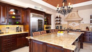 Una cocina amplia con armarios de madera oscura, una isla grande con encimera de granito y una lámpara de araña clásica.