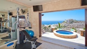 Un gimnasio con equipo de ejercicios y vistas a una piscina y al océano.