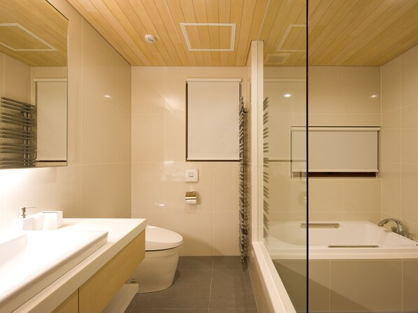 Un baño moderno con inodoro, ducha con mampara de vidrio y bañera.