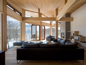 Amplia sala de estar con un sofá modular grande, vigas de madera y ventanas amplias que ofrecen vistas al exterior.