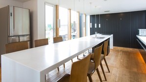 A modern kitchen with a long white countertop, wooden chairs, and pendant lighting.