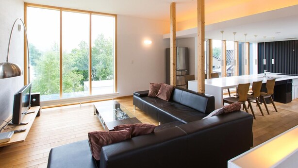 A modern living room with a large window, a black sofa, a coffee table, and a dining area with chairs and a table.