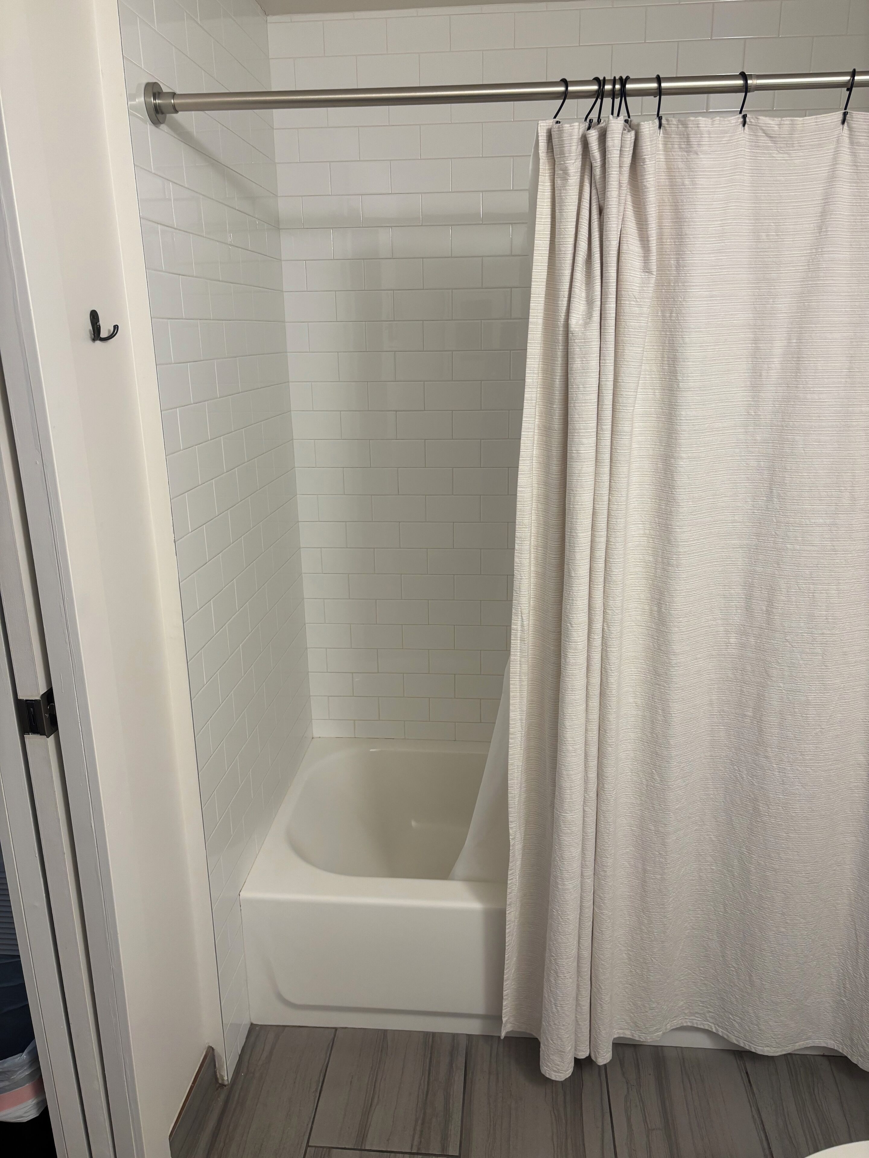 Un baño con pared de ducha en blanco y azulejos, una bañera blanca y suelo de madera.