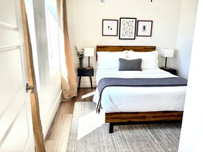 A hotel room with a wooden bed, white bedding, a grey throw, a nightstand with a lamp, and three framed artworks on the wall. - Cozy Modern Apt Downtown Tulsa-Gym Access (Tulsa)