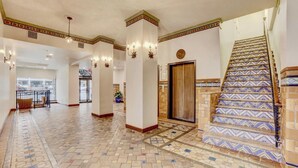 Un hall d’entrée spacieux avec un sol à motifs, un escalier orné de carreaux décoratifs et une colonne centrale illuminée.