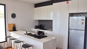 Eine moderne Küche mit weißen Schränken, einem Edelstahlkühlschrank, einer schwarzen Kaffeemaschine und einem Holzer Schneidebrett mit Messern.