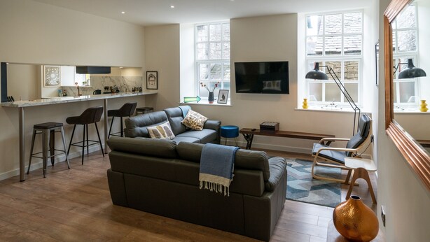 A spacious living area with a dark green sofa, a kitchen area with a bar, and a large window providing natural light. - Two separate 2-bedroom apartments, joined by a private hallway. Kendal Town Centre (Kendal)