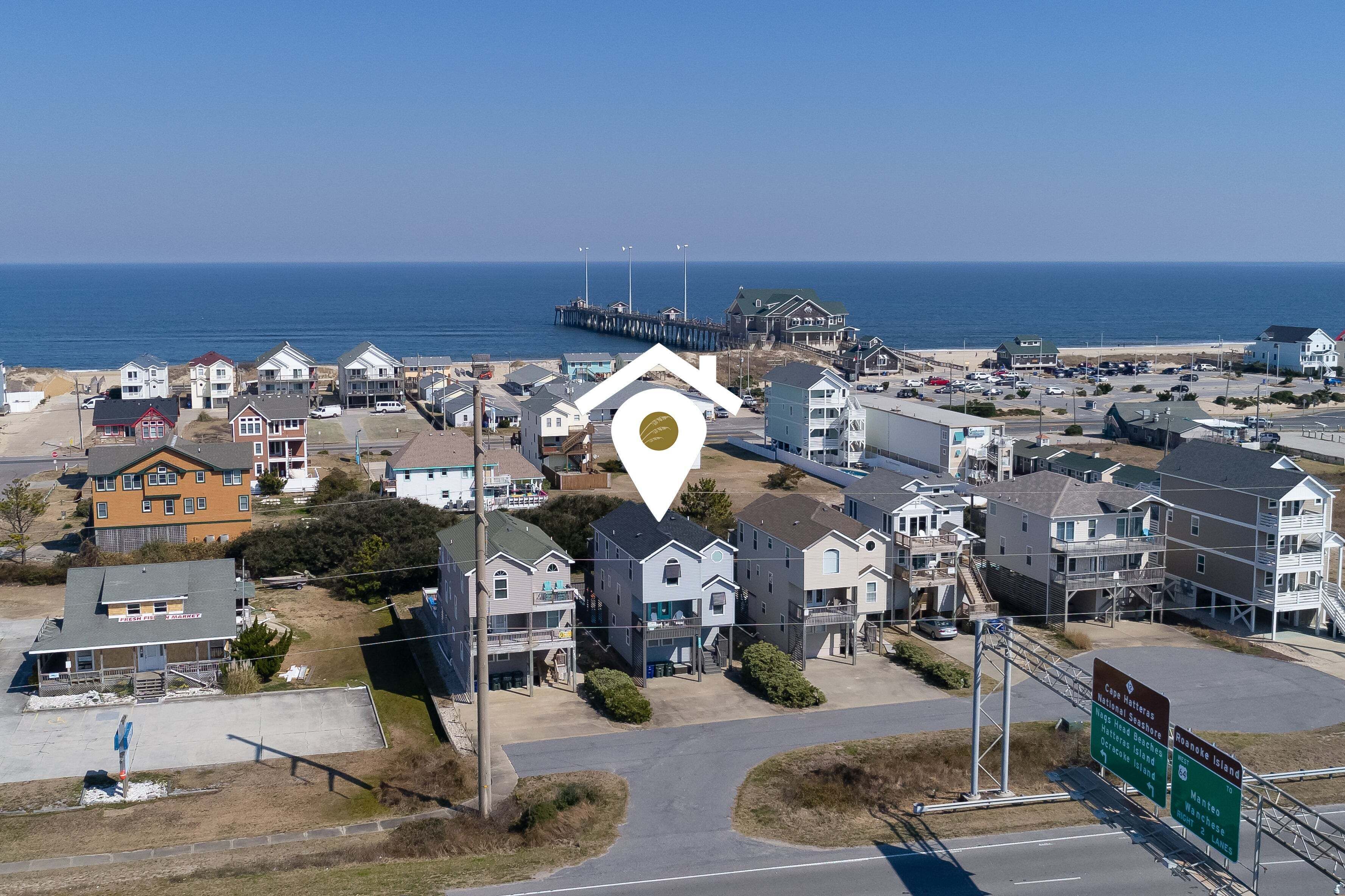 A coastal residential area with houses, a pier, and a clear view of the ocean.