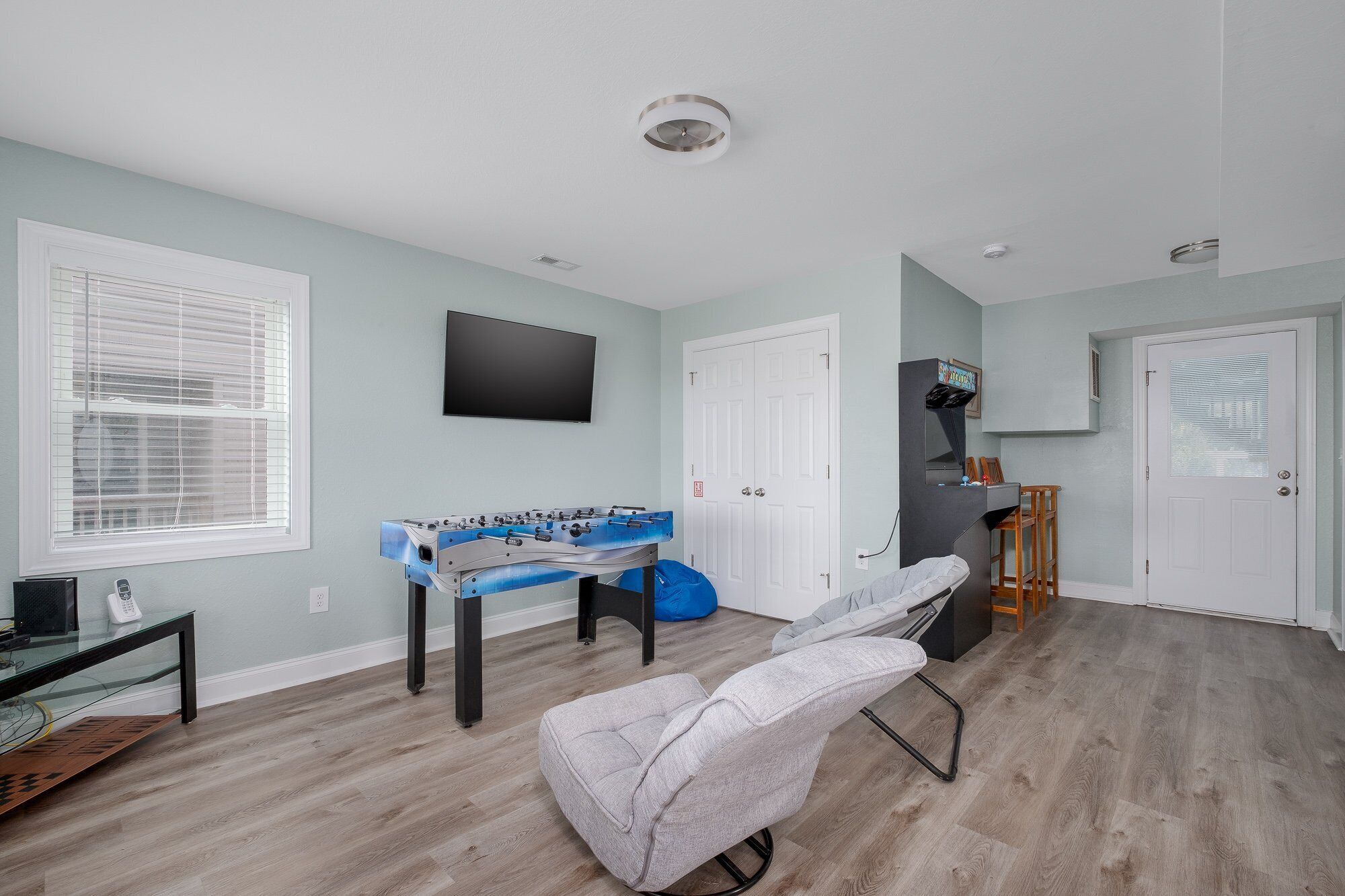 A room with a foosball table, a TV mounted on the wall, and a door with a window.