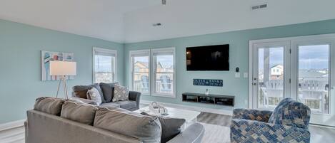 A living room with a grey sofa, a patterned armchair, a ceiling fan, and a TV on the wall.