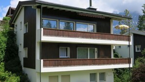 Un bâtiment à deux étages doté d’un balcon, d’une cheminée et d’une pile de bois de chauffage à l’extérieur.