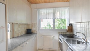 Une cuisine compacte avec des meubles en bois, un four encastré, un évier et une fenêtre avec des rideaux.