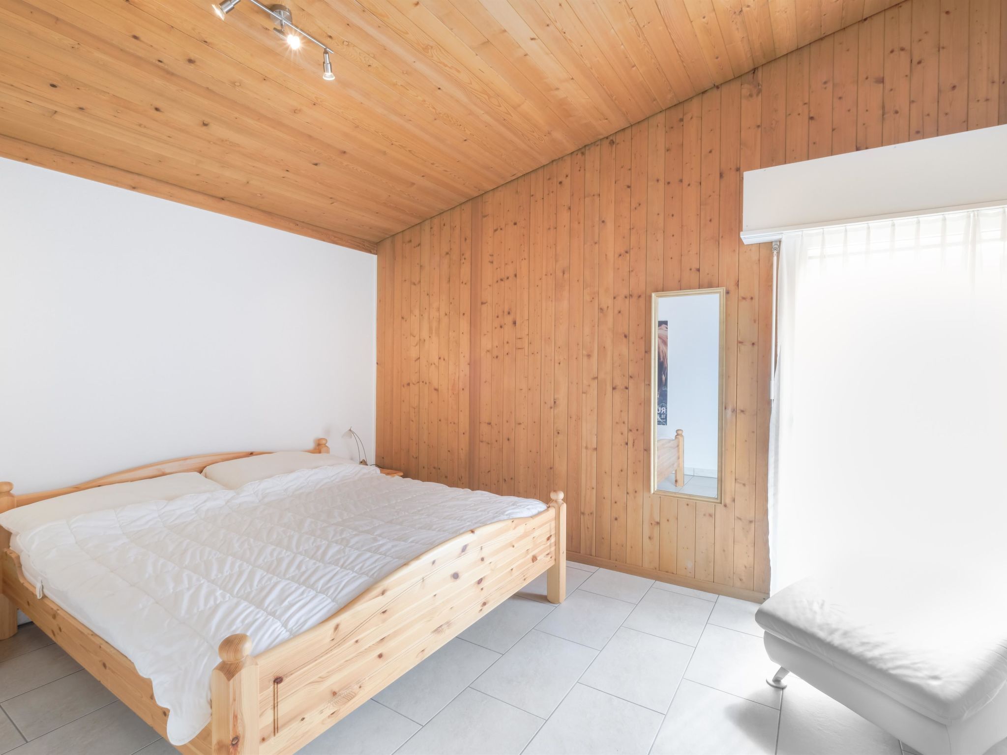 A bedroom with a wooden bed frame, white bedding, and a large window with curtains.