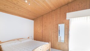 Une chambre à coucher avec un cadre de lit en bois, du linge de lit blanc et une grande fenêtre avec des rideaux.