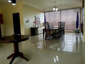 A spacious room with a round table and chairs, a kitchenette, and large windows with blinds. - Canoy's Canyon Apartelle in Dalaguete Cebu (Dalaguete)