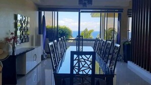 Ein Essbereich mit einem großen Tisch, Stühlen, einem Deckenventilator und Blick auf den Ozean.