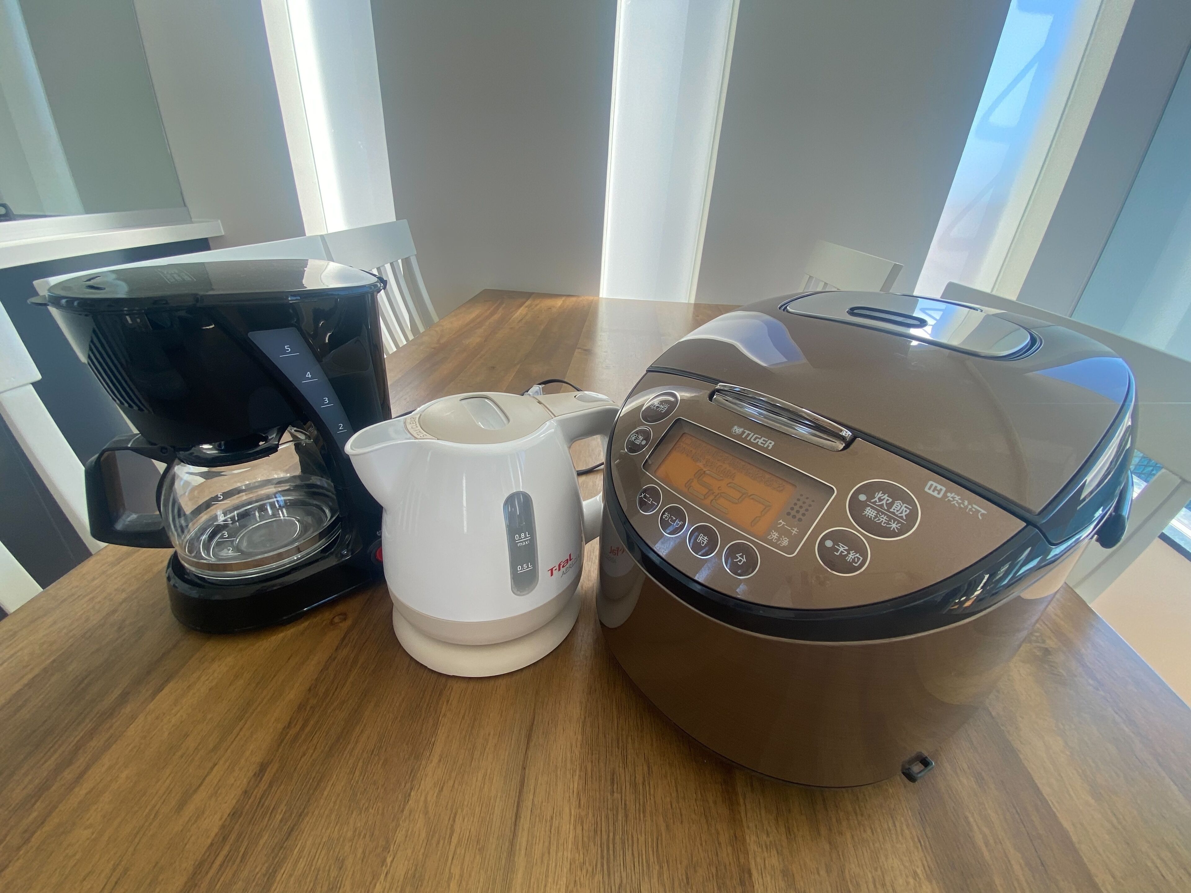 A kitchen with a coffee maker, a kettle, and a rice cooker on a wooden table.