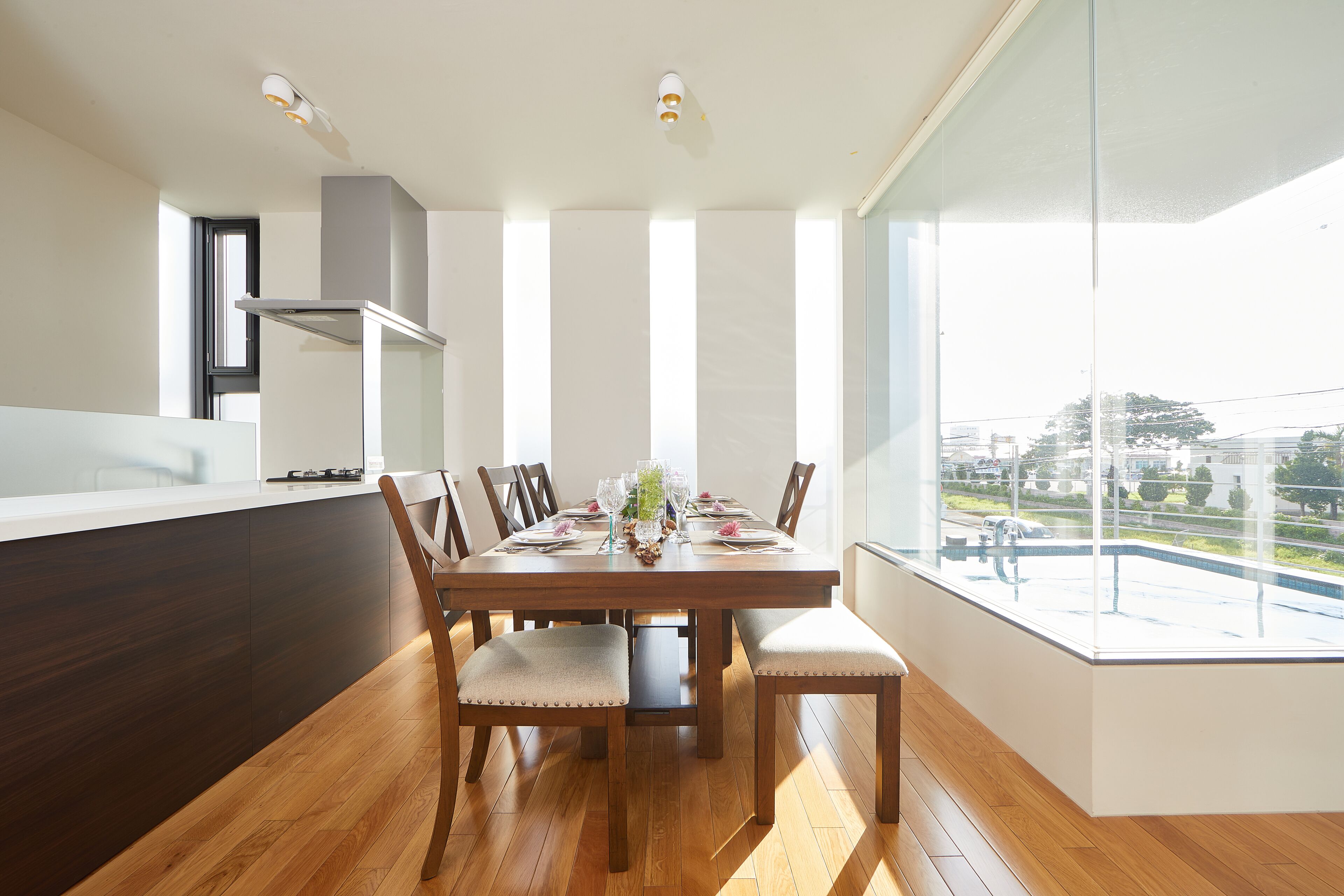 A modern dining area with a wooden table set for six, surrounded by upholstered chairs. A large window offers a view of the outdoors.