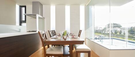 A modern dining area with a wooden table set for six, surrounded by upholstered chairs. A large window offers a view of the outdoors.