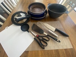 Una encimera de cocina con una tabla de cortar, un batidor, una espátula, un cuchillo, un par de tijeras, una sartén y una olla.